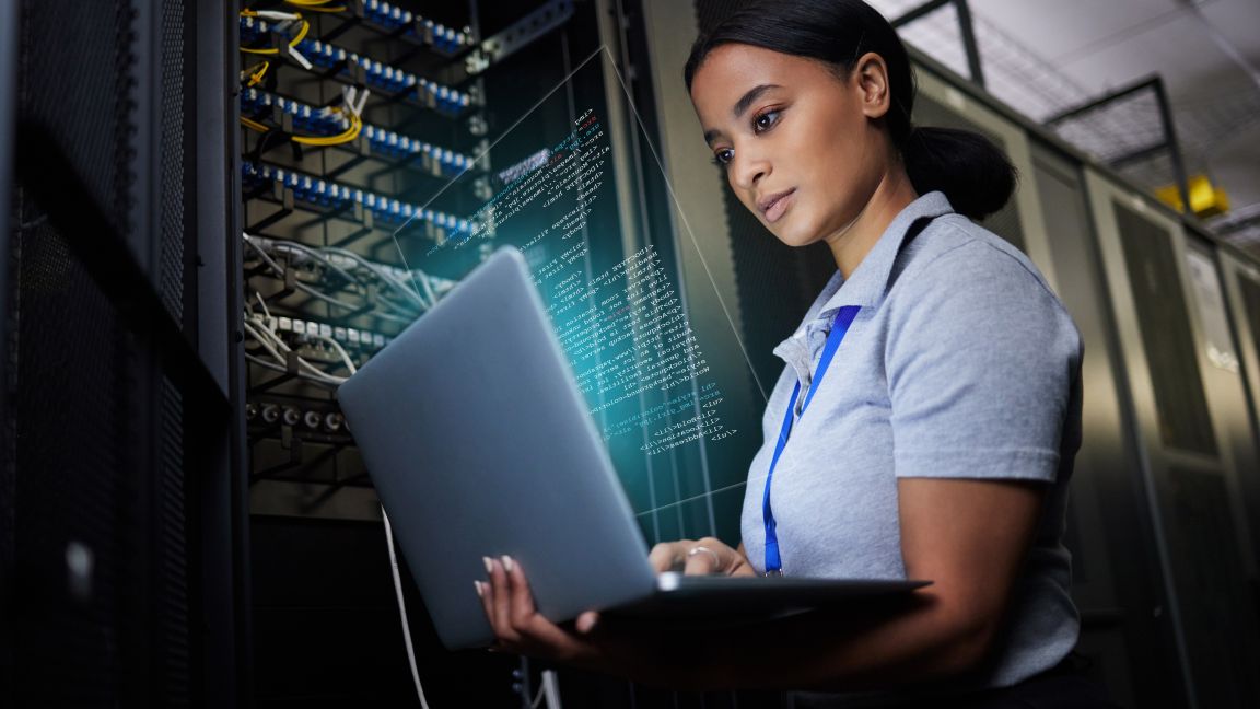 Person arbeitet mit einem Laptop in einem Serverraum und analysiert Datenströme und digitale Systeme.